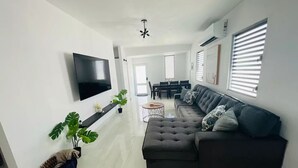 A modern living room with a sectional sofa, a flat-screen TV, and a dining area with a table and chairs. - Casa LindaMaria 4 mins from the airport 6 mins from isla verde (Carolina)