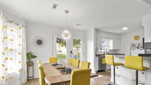 Une cuisine moderne avec des meubles blancs, un évier en acier inoxydable et un coin repas comprenant une table en bois et des chaises jaunes.
