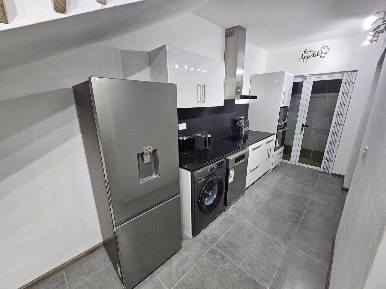 A modern kitchen with stainless steel appliances, a built-in washing machine, and a black countertop.