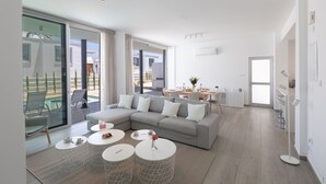 A modern living room with a grey sectional sofa, white round coffee tables, and a glass sliding door leading to a balcony. - Protaras Olivine Villa OL9 - Beautiful 4BDR Protaras Villa with Private Pool (Protaras)
