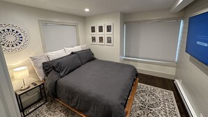 A modern bedroom with a large bed, a bedside table with a lamp, a decorative wall piece, and a TV on the wall. - Updated Canyons condo steps from Cabriolet lift - full kitchen, washer/dryer (Park City)