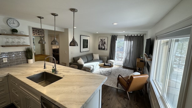 A modern kitchen with a large island, a dining area with a sofa, and a living room with a TV and a large window. - Updated Canyons condo steps from Cabriolet lift - full kitchen, washer/dryer (Park City)