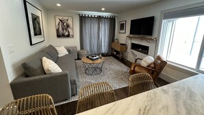 A modern living room with a grey sofa, a coffee table, wicker chairs, a fireplace, and a TV. - Updated Canyons condo steps from Cabriolet lift - full kitchen, washer/dryer (Park City)