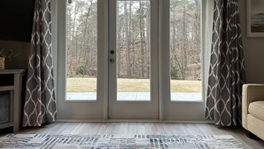 Quarto com porta de vidro deslizante para um quintal, tapete estampado e sofá bege.