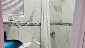 A bathroom with a white toilet, a blue vessel sink, a shower with a white curtain, and a tiled backsplash. - The Sunset Stay BnB (Nassau)