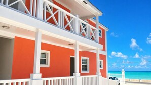 A two-story building with a balcony, white railings, and a view of the ocean.