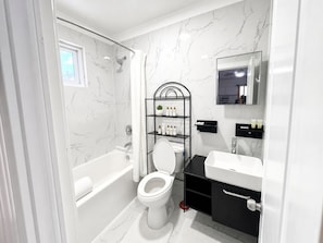 A bathroom with a bathtub, toilet, and a vanity with a mirror. - The Sunset Stay BnB (Nassau)