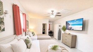A hotel room with two beds, a TV, a ceiling fan, a plant, and a view of the beach. - The Sunset Stay BnB (Nassau)