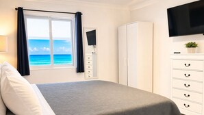 A bedroom with a bed, a wardrobe, a TV, and a view of the ocean. - The Sunset Stay BnB (Nassau)