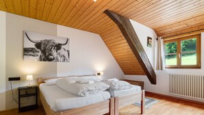 Een slaapkamer met een houten plafond, een bed met witte beddengoed, een zwart-wit kunstwerk, een nachtkastje en een raam met uitzicht op groen.