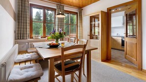 Een eethoek met een houten tafel, stoelen, een bank en uitzicht op het omliggende landschap door grote ramen.