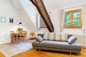 A loft-style room with a gray sofa, wooden dining table, and chairs. There is a window with curtains, a radiator, and a slanted ceiling beam. - Holiday Home 'Haus 2 Hanselishof - 2 Wohnungen' with Mountain View, Shared Garden and Wi-Fi (Schenkenzell)
