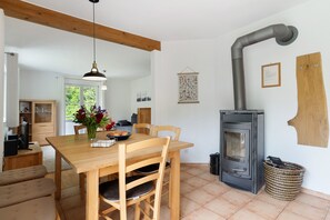 Un coin repas avec une table et des chaises en bois, un vase avec des fleurs, un poêle et un élément décoratif suspendu au mur.
