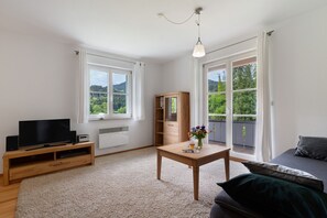 Un salon moderne avec un téléviseur, un meuble de rangement en bois, une table avec un vase et un canapé.