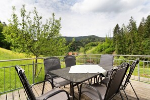 Une terrasse extérieure avec une table et des chaises, offrant une vue sur un paysage verdoyant, avec des arbres et des collines.