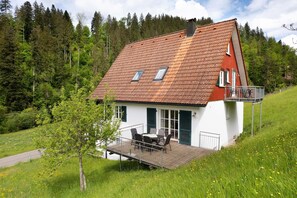 Une maison avec un toit en pente, un balcon et une petite terrasse aménagée avec du mobilier d’extérieur.