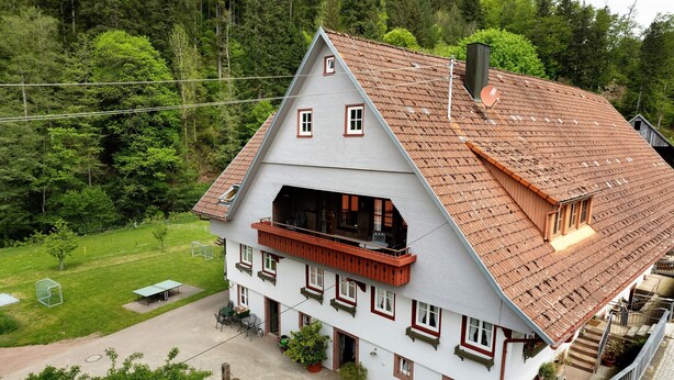 Une maison à deux étages avec un toit en pente, un balcon et un petit jardin.