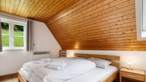 Une chambre avec un plafond en bois, un lit avec une literie blanche, une table de chevet avec une lampe et une fenêtre avec des rideaux.