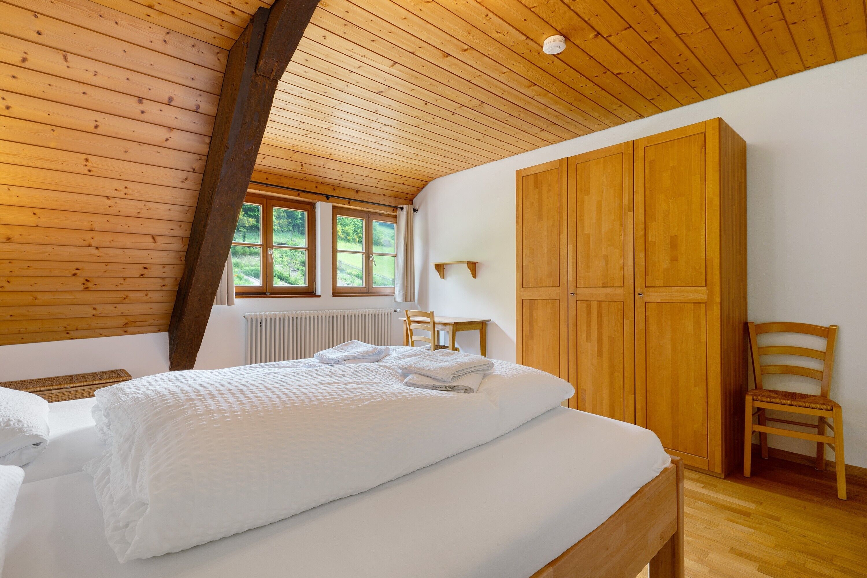 Ein Schlafzimmer mit Holzboden, einem Bett mit weißen Leinen, einem Holzschrank und einem Stuhl.