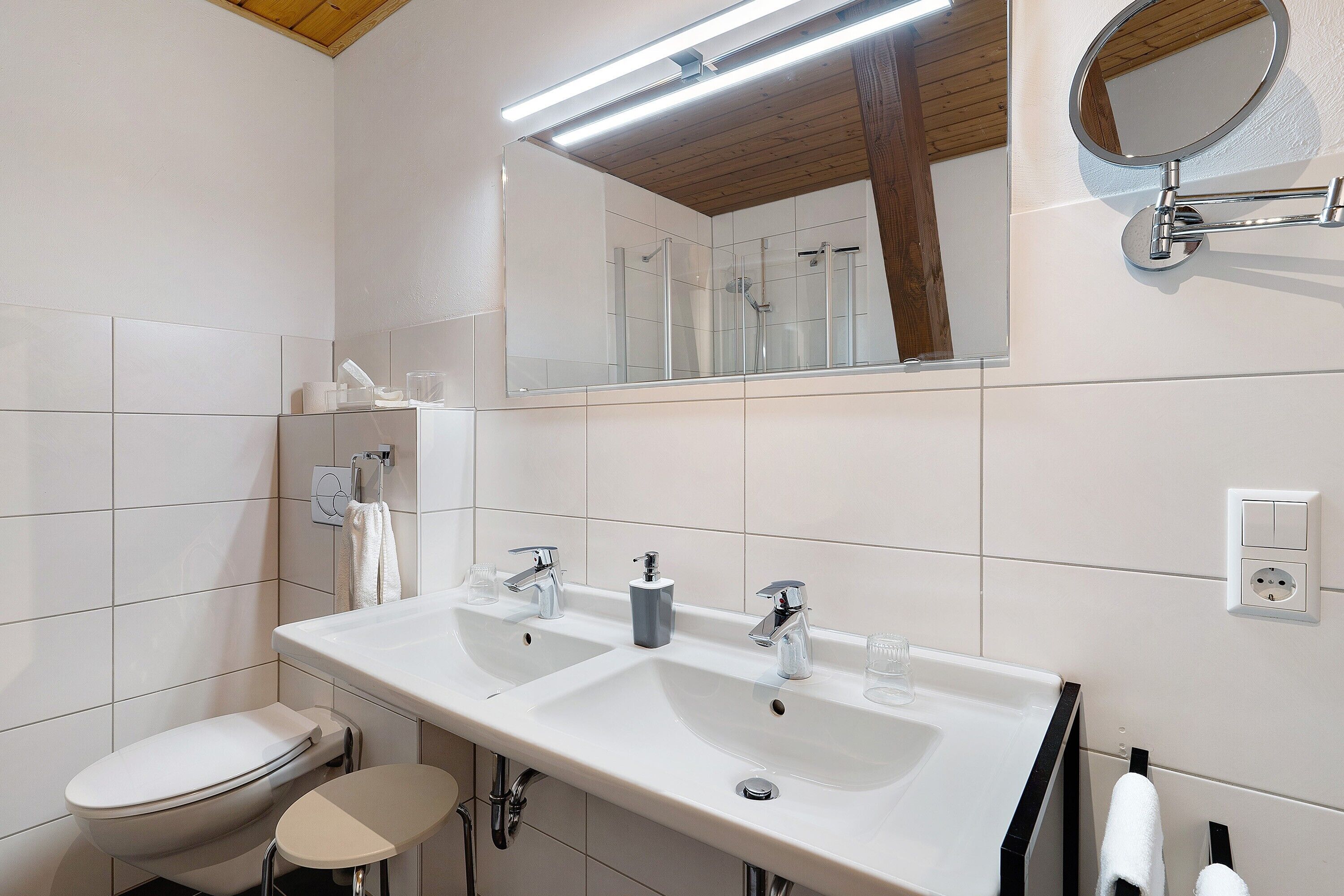 A modern bathroom with a white sink, two faucets, a toilet, and a mirror.