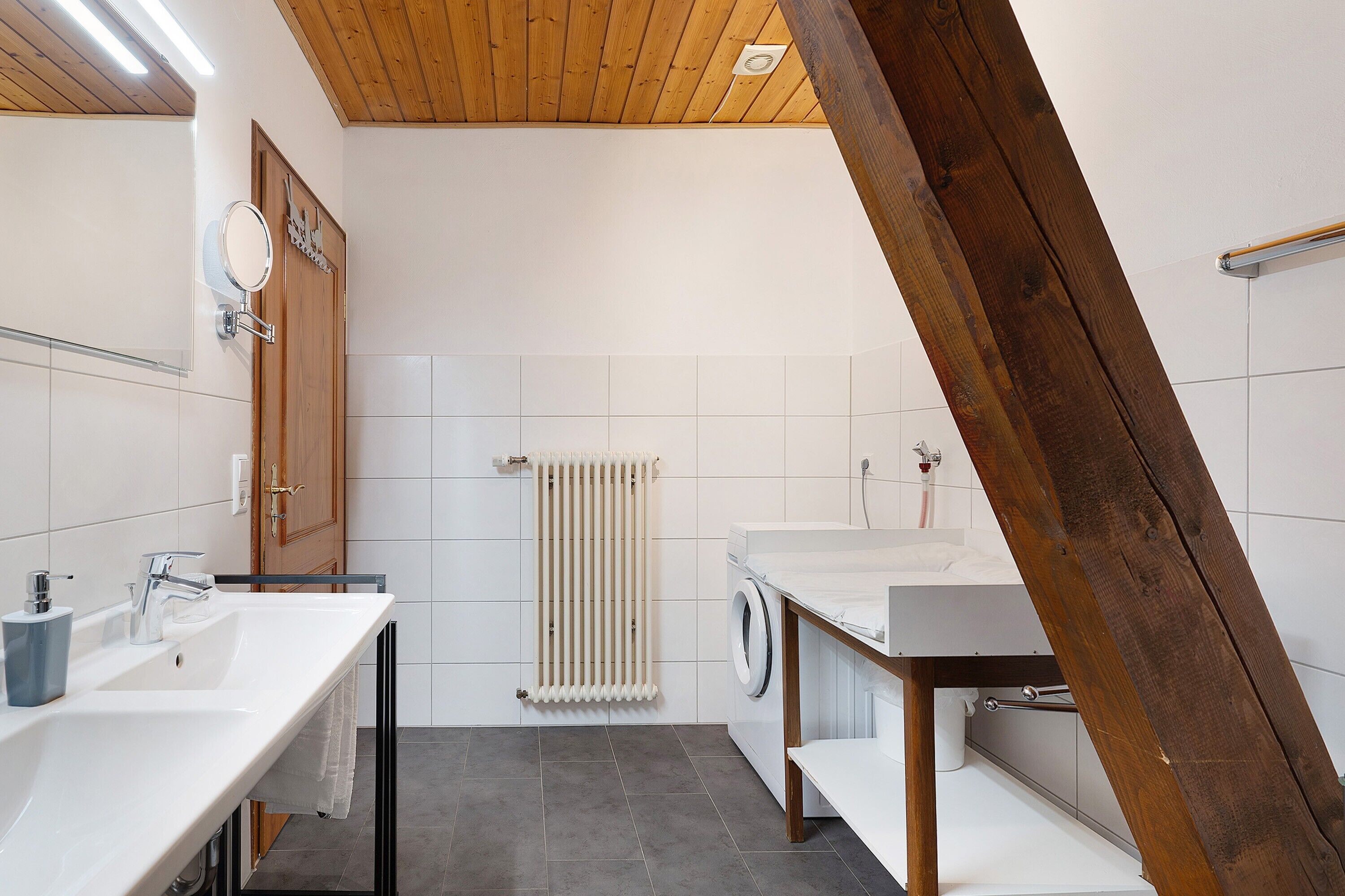 Un baño moderno con techo de madera, lavadora, lavamanos y espejo.