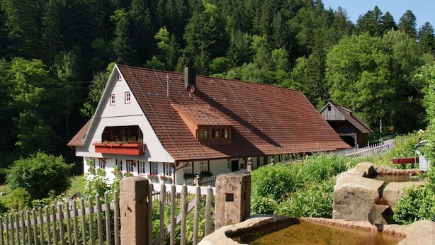 A traditional chalet with a red-tiled roof, a white exterior, and a wooden fence.