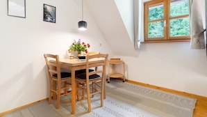 A dining area with a table, chairs, a hanging light, and a window with curtains.