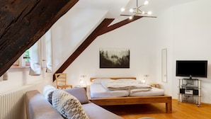 A bedroom with a bed, a sofa, a TV, and a painting on the wall.