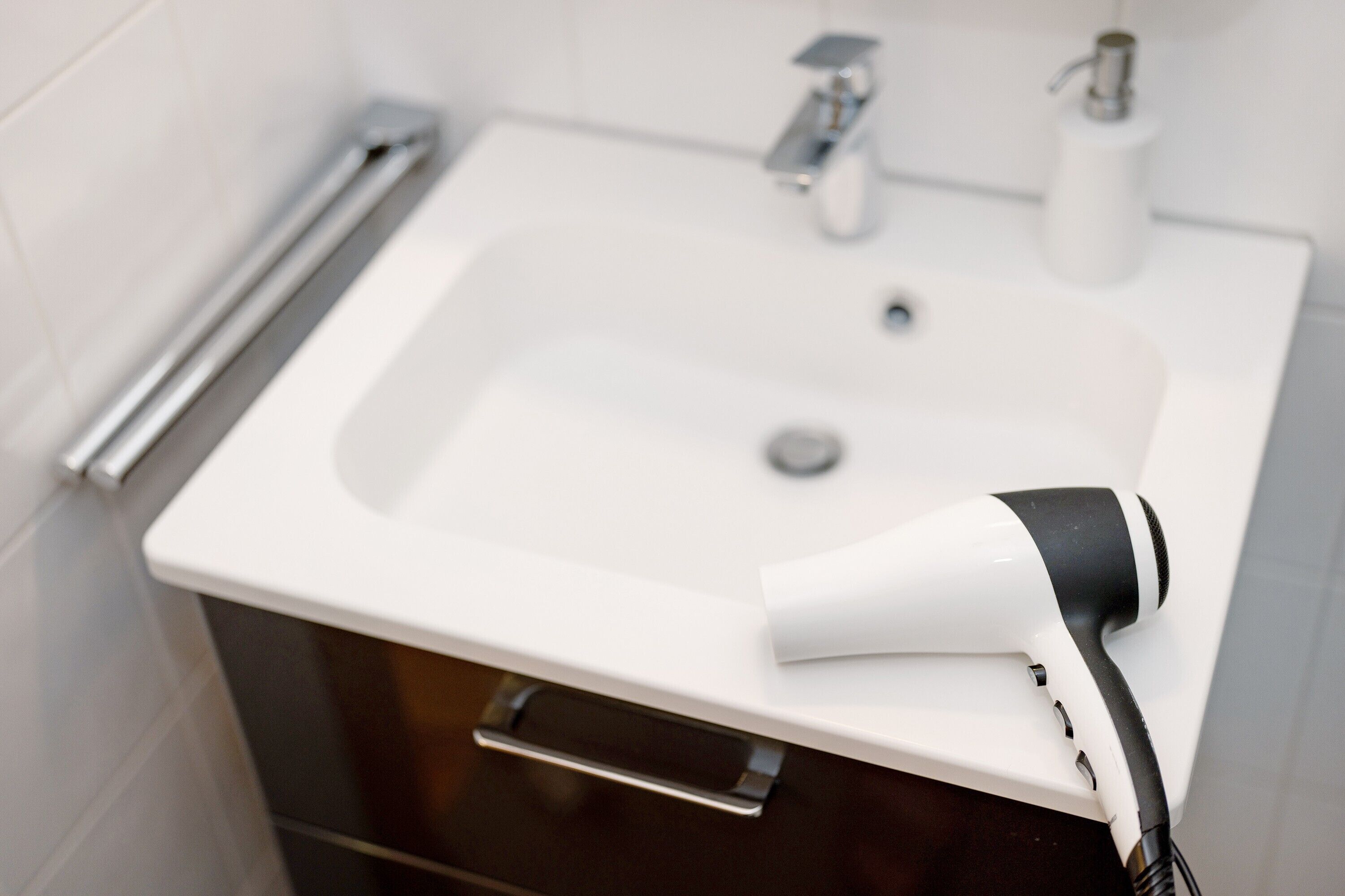 A bathroom with a white sink, a handheld hair dryer, and a towel rack.