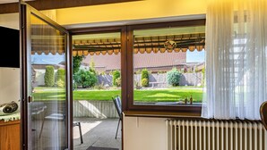 Una habitación con puerta de cristal corredera que da a un jardín, un radiador y un televisor a la izquierda.