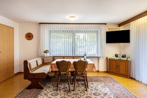 Un área de comedor con una banca, sillas, una mesa, un televisor y un armario.