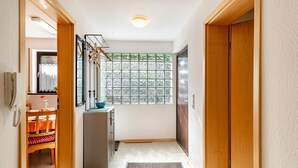 Un pasillo con puerta de madera, ventana con vistas, lavamanos y una pequeña mesa con silla.