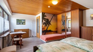 A room with a wooden ceiling, a bed with a patterned bedspread, a desk with a chair, and a wall with a sunset and palm tree mural. - Haus Berger Ferienwohnung 2 (Wehr)