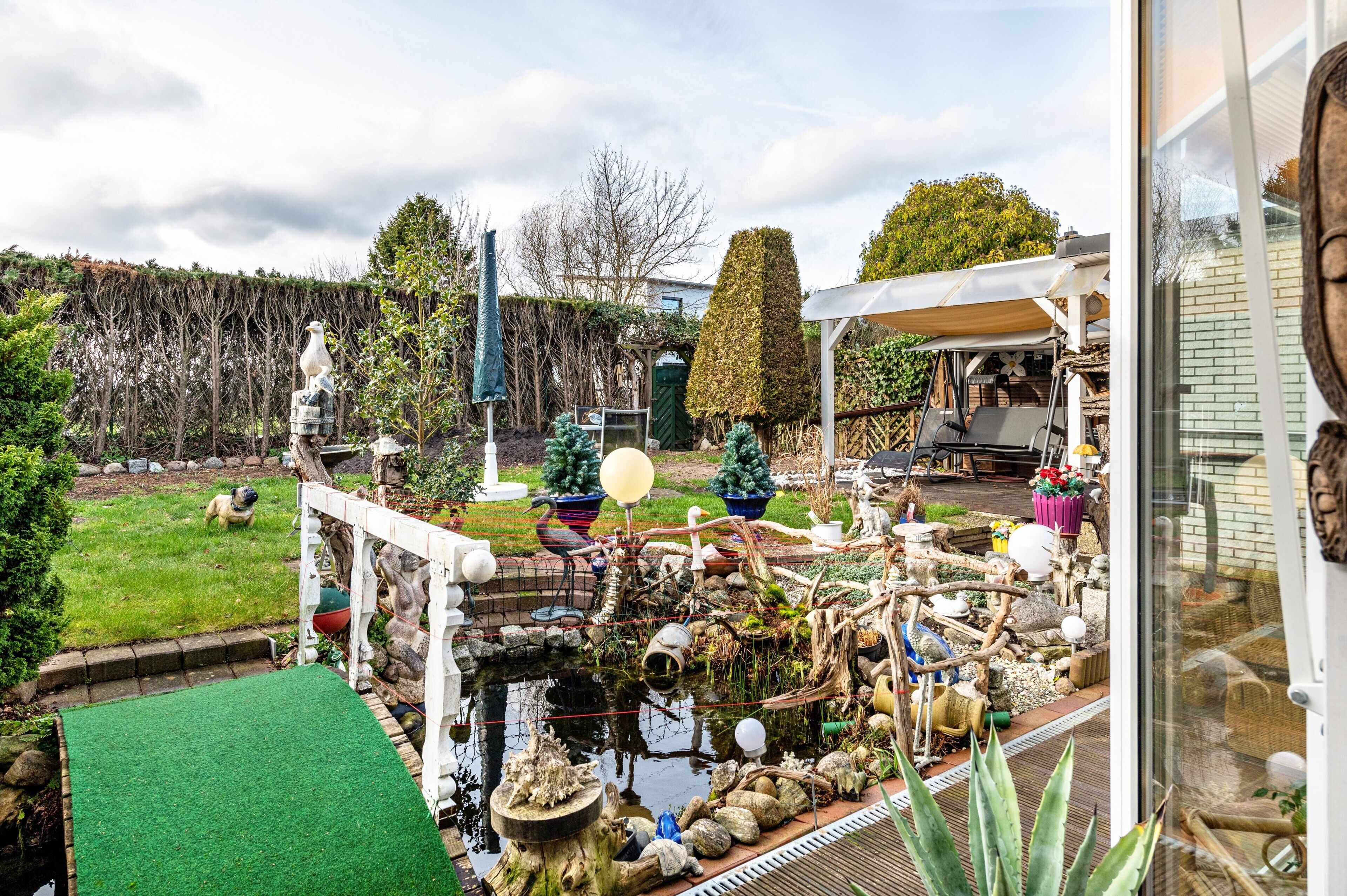 Ein Garten mit Teich, Statue und verschiedenen Pflanzen.