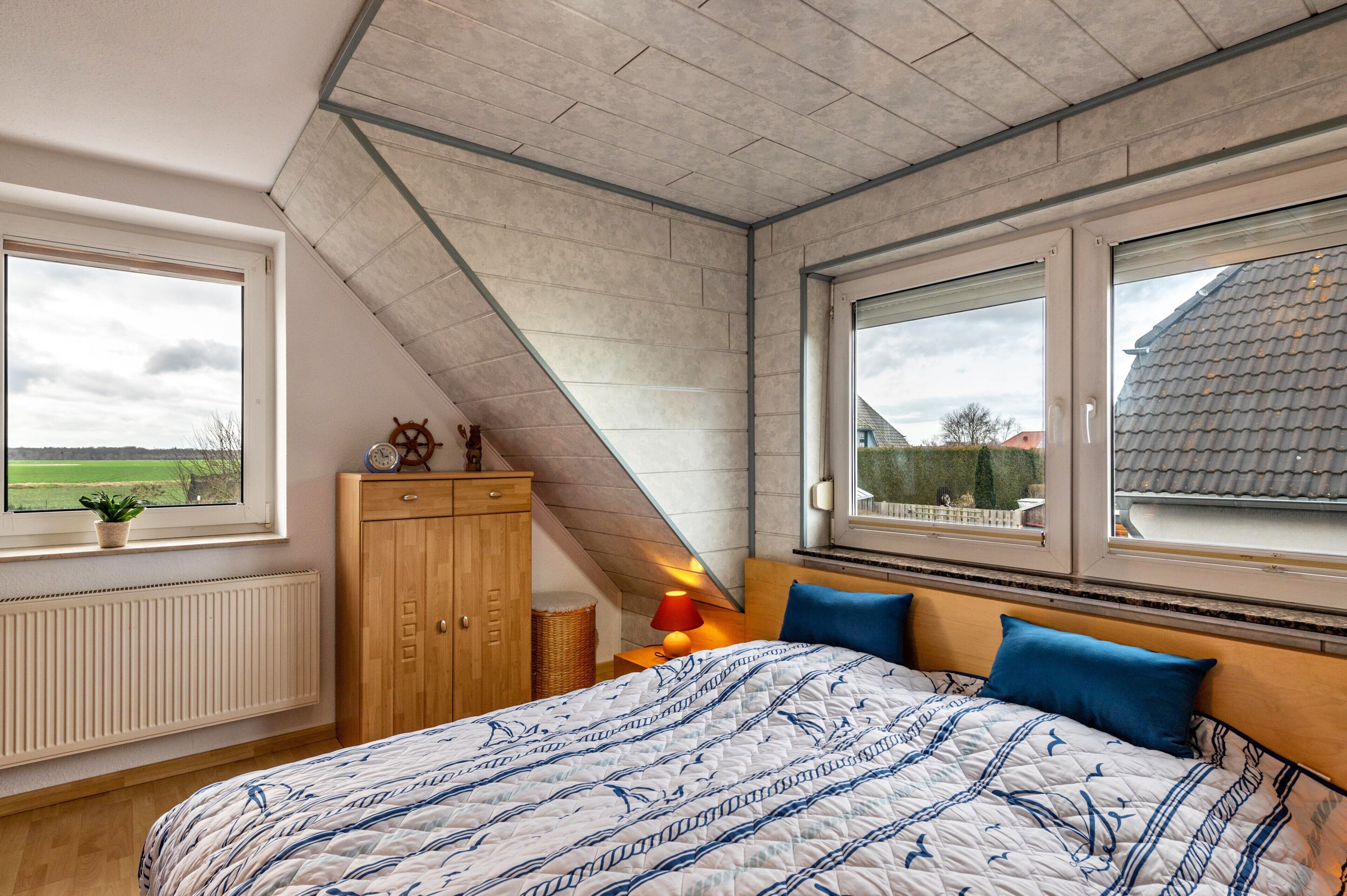 Een slaapkamer met een groot bed, twee ramen, een houten garderobe en een radiator.