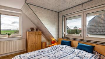 Een slaapkamer met een groot bed, twee ramen, een houten garderobe en een radiator.