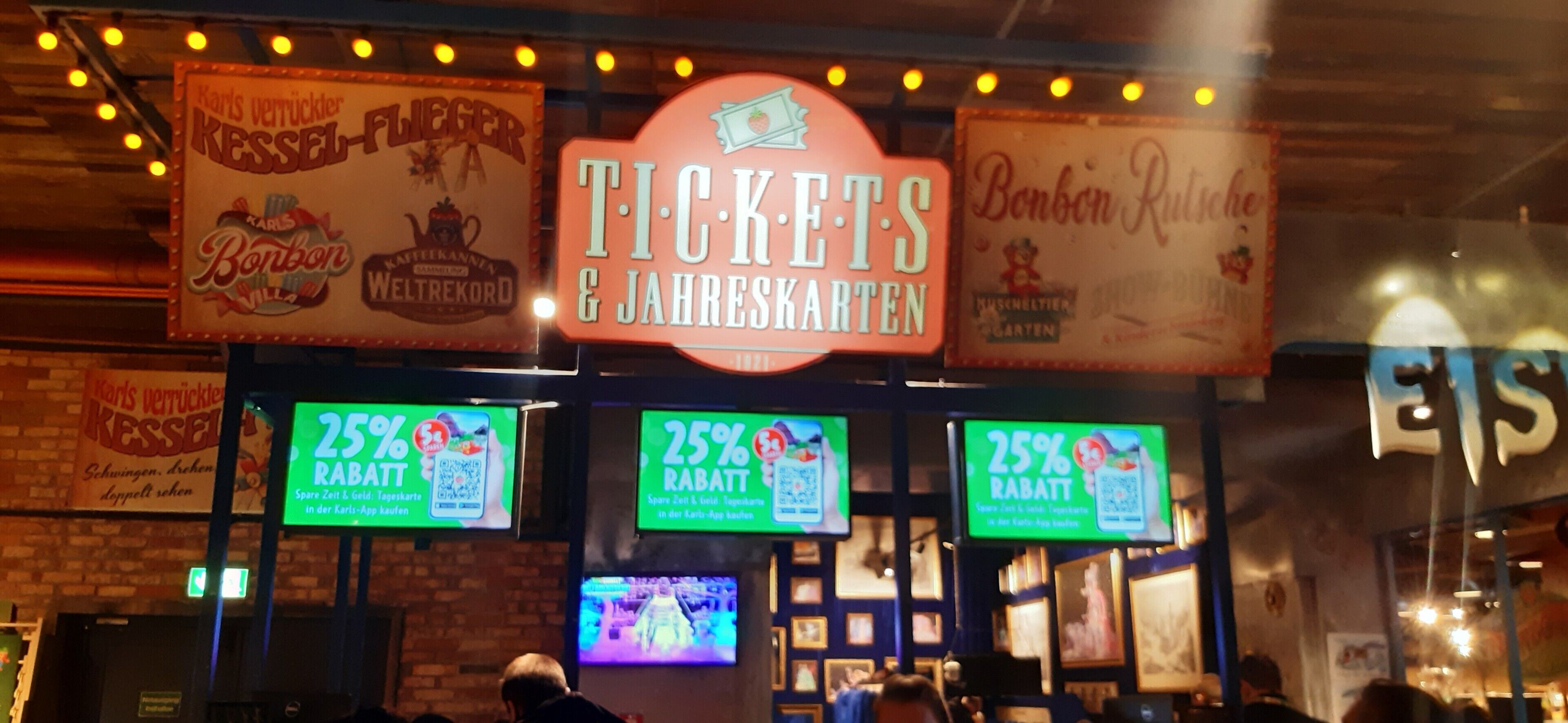 A ticket booth with signs for 'Tickets & Yearbooks' and '25% Rabatt' offers.