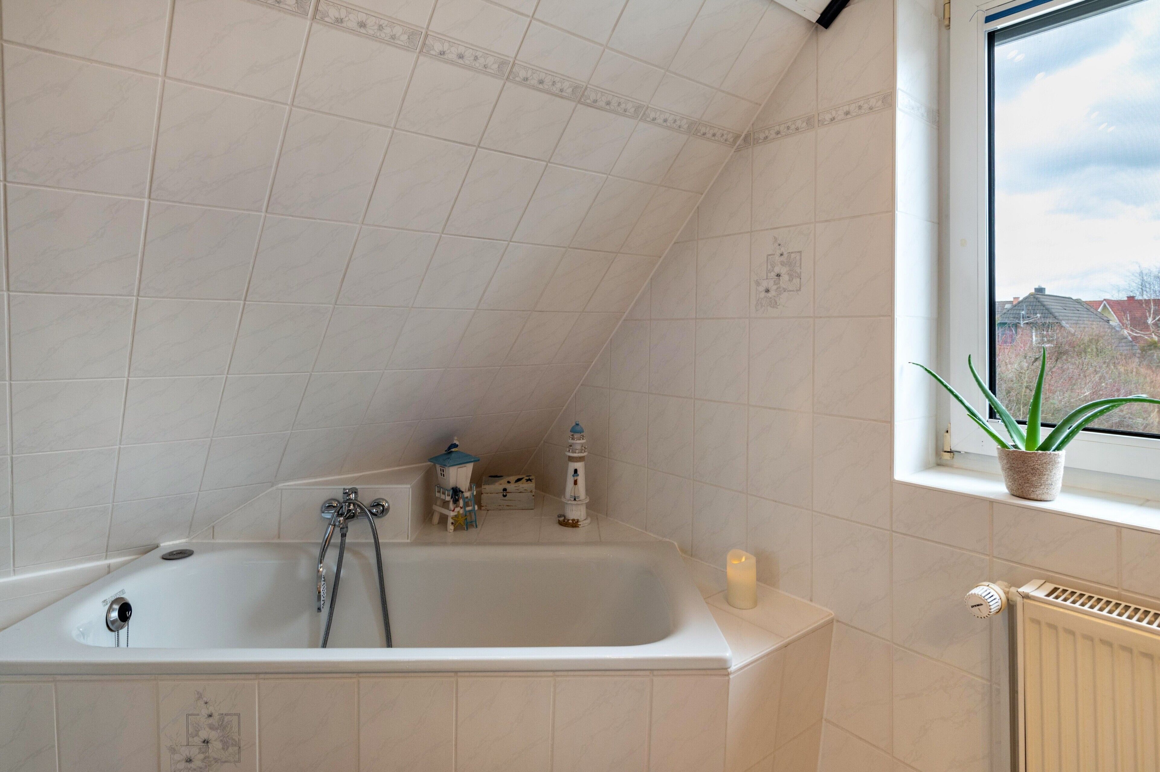 Ein Badezimmer mit einer Badewanne, einem Fenster mit Pflanze und einer Heizung.