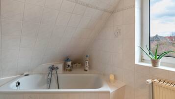 Ein Badezimmer mit einer Badewanne, einem Fenster mit Pflanze und einer Heizung.
