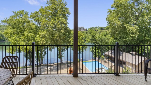 A wooden deck with a view of a lake, a pool, and a building in the background. - Lakefront Retreat on Lake Taneycomo, Near Branson Landing and Attractions (Branson)