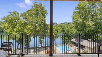 A wooden deck with a view of a lake, a pool, and a building in the background.