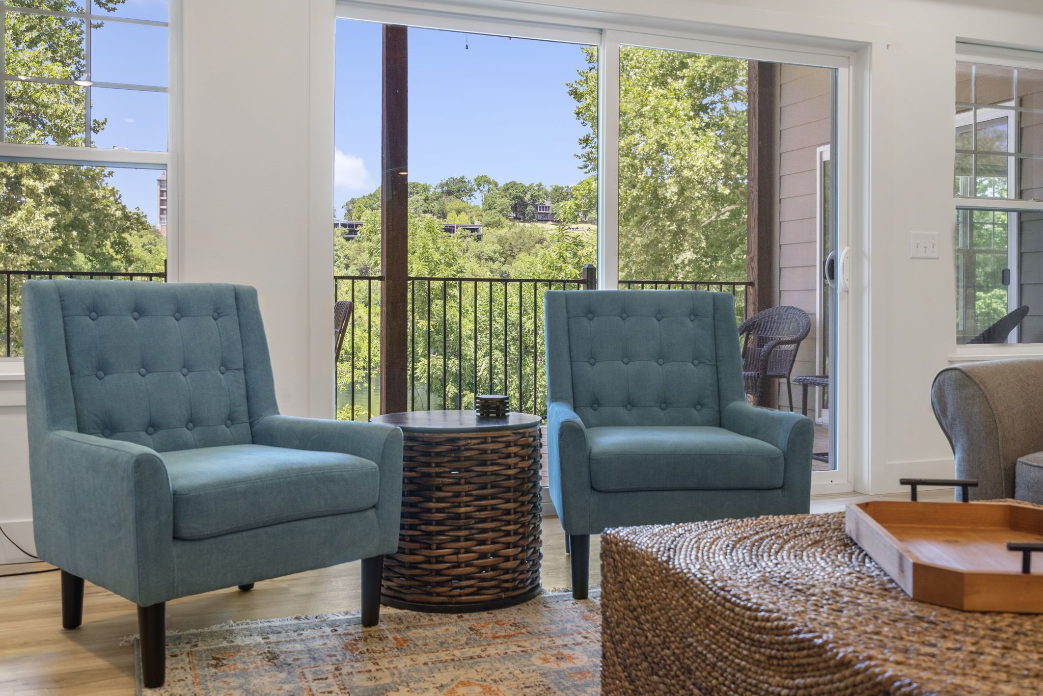 A balcony with two blue armchairs, a wicker side table, and a woven ottoman.