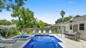 A swimming pool with multiple lanes, surrounded by lounge chairs and a patio area with a table and chairs.