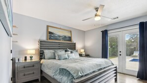 A bedroom with a bed, bedside tables, a ceiling fan, and a view of the outdoors.