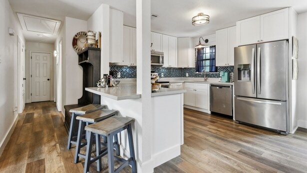 A modern kitchen with white cabinets, stainless steel appliances, and a wooden island with bar stools.