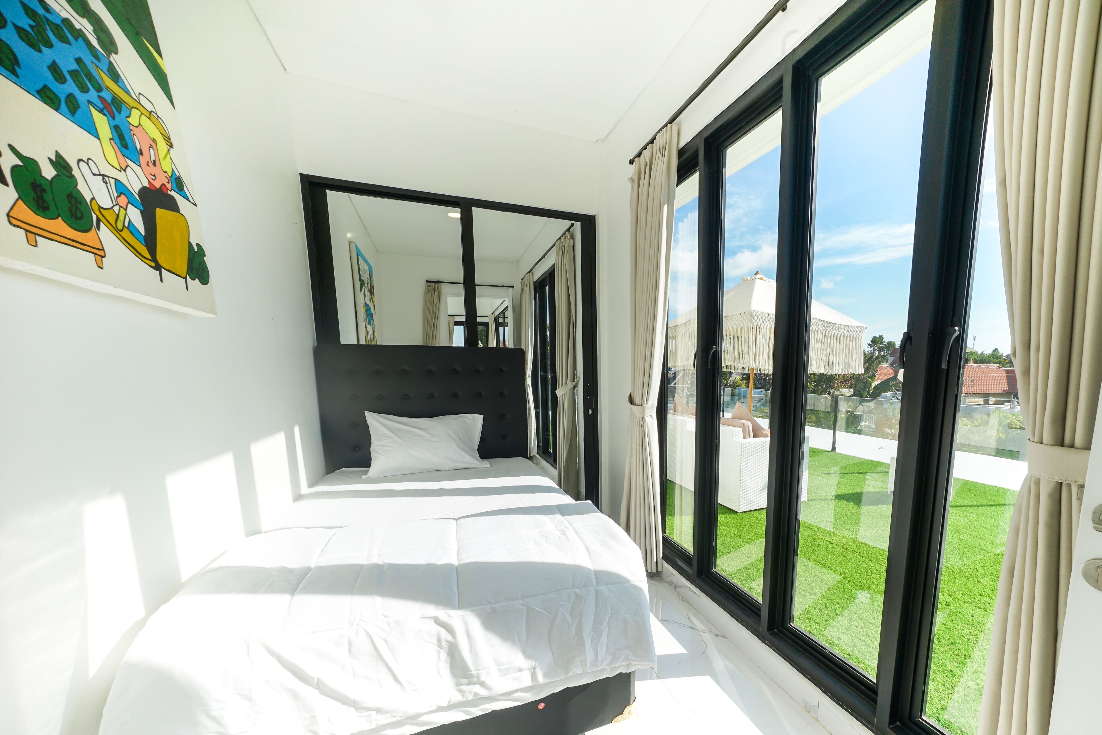 A bedroom with a large bed, a mirror, and a sliding glass door leading to a balcony.