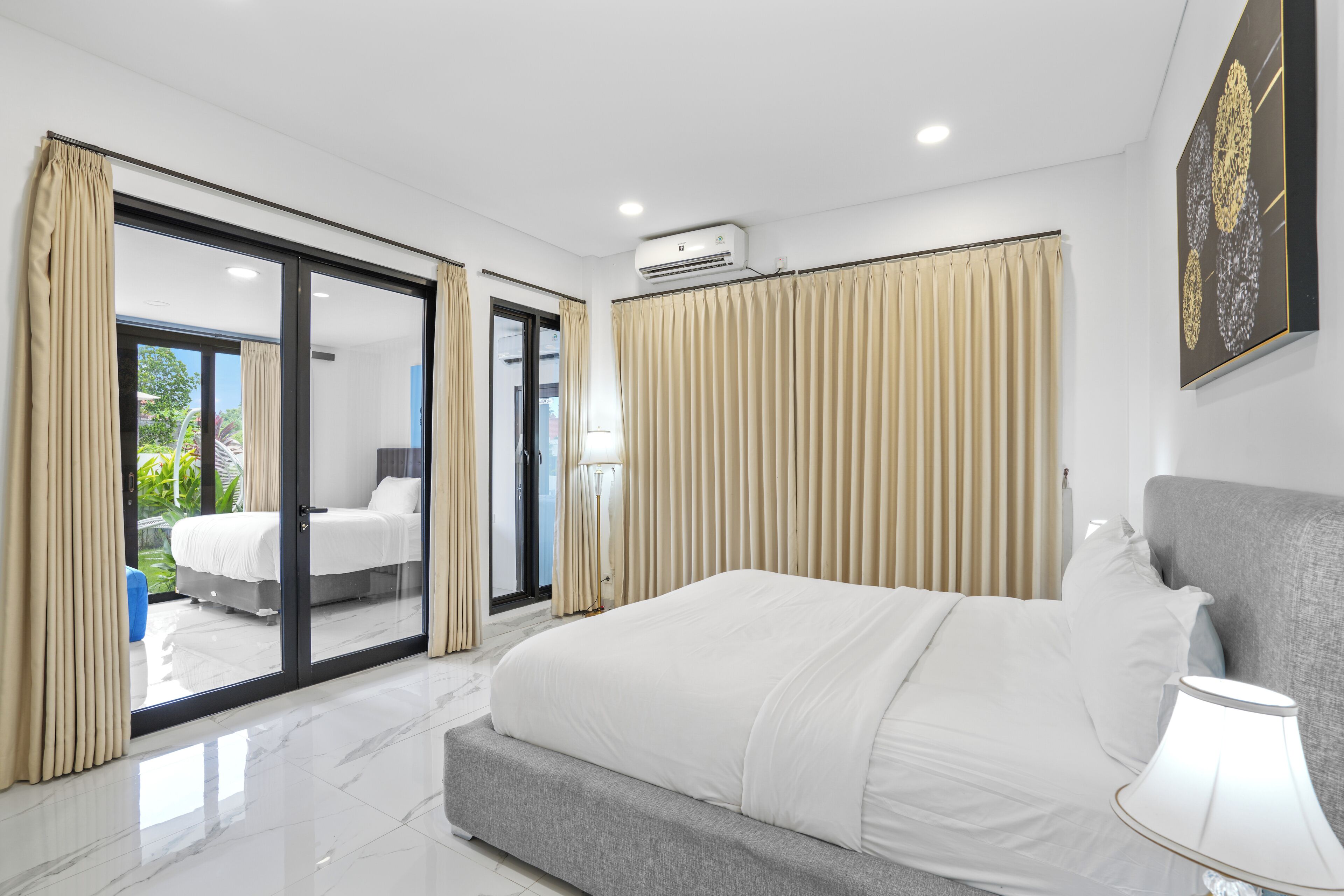 A modern hotel room with a large bed, sliding glass doors to a balcony, and a ceiling-mounted air conditioner.