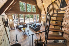 A spacious loft-style room with a large window, a cozy seating area, and a spiral staircase. - Shaver Wood Forrest-Smokey Tree (Shaver Lake)