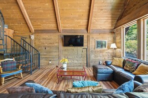 Un interior rústico con una escalera de madera, un sofá de cuero, una mesa de centro y un televisor montado en la pared.