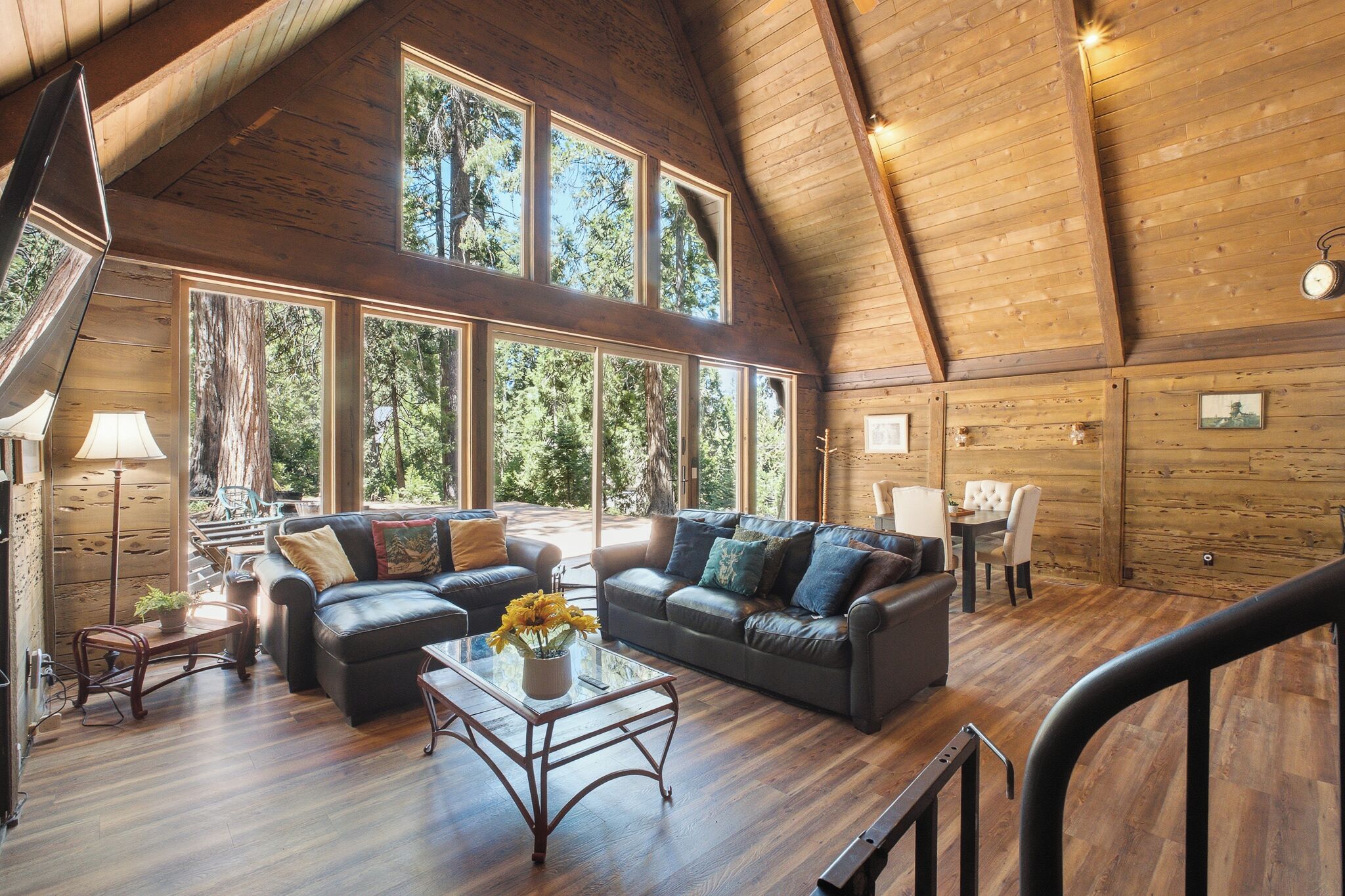 A spacious living area with a high ceiling and large windows, featuring a sofa set and a dining table.